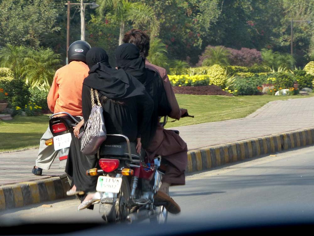 Two women riding side saddle behind the motorbike driver.